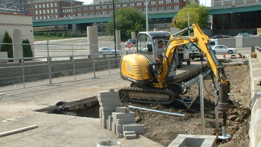 An image of an excavator digging dirt cut out of concrete at a commercial site
