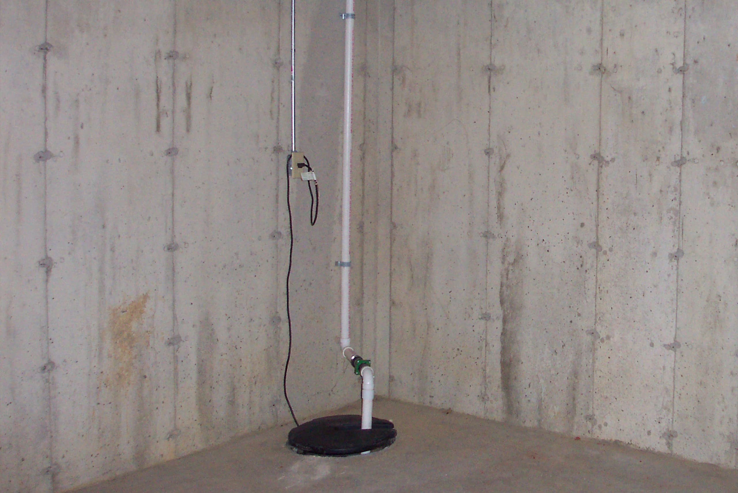 a picture of a basement with a tall water pipe going into a drain in a residential home