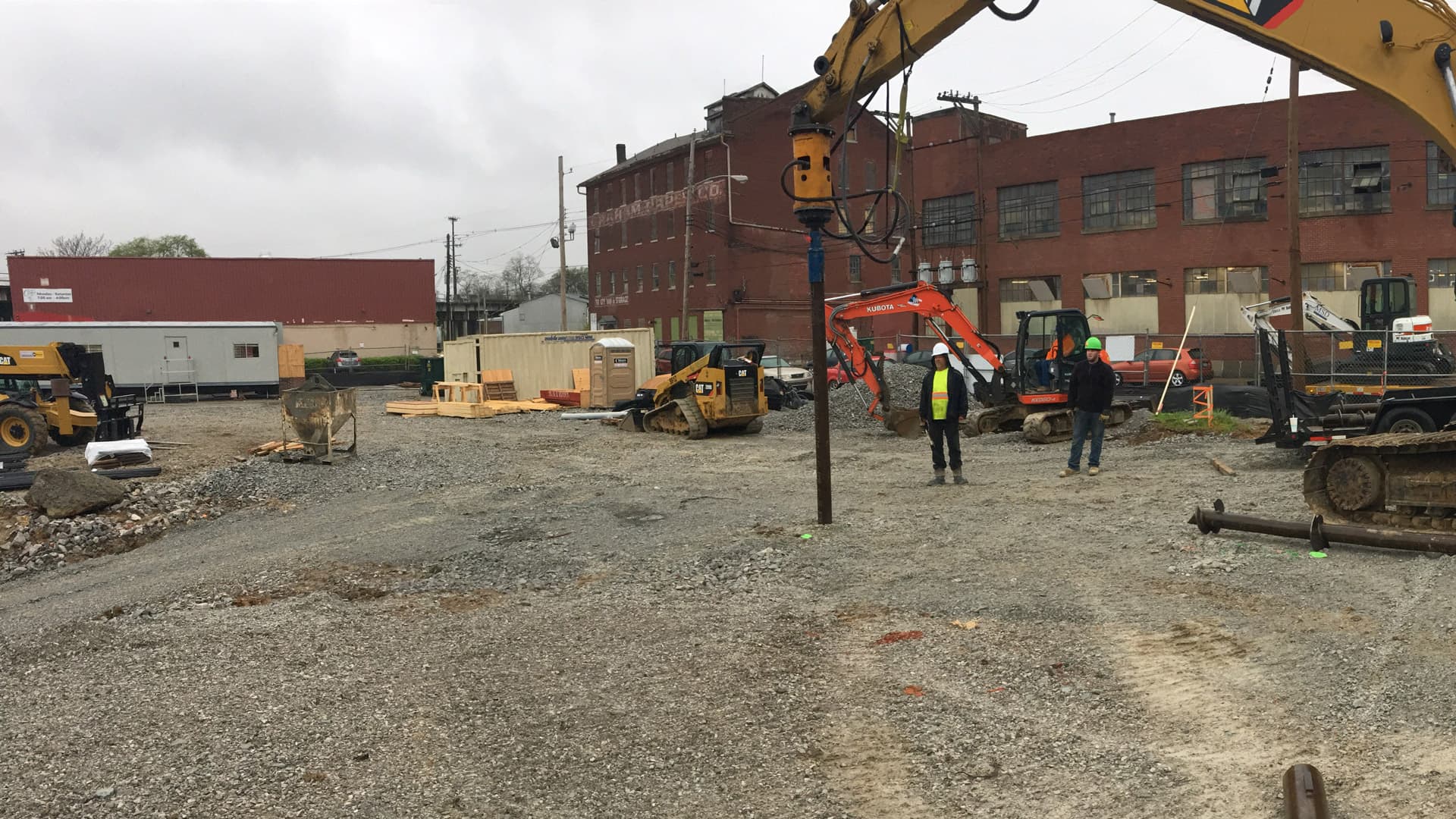two workers at a commercial site watching a drill put driven piles into the ground