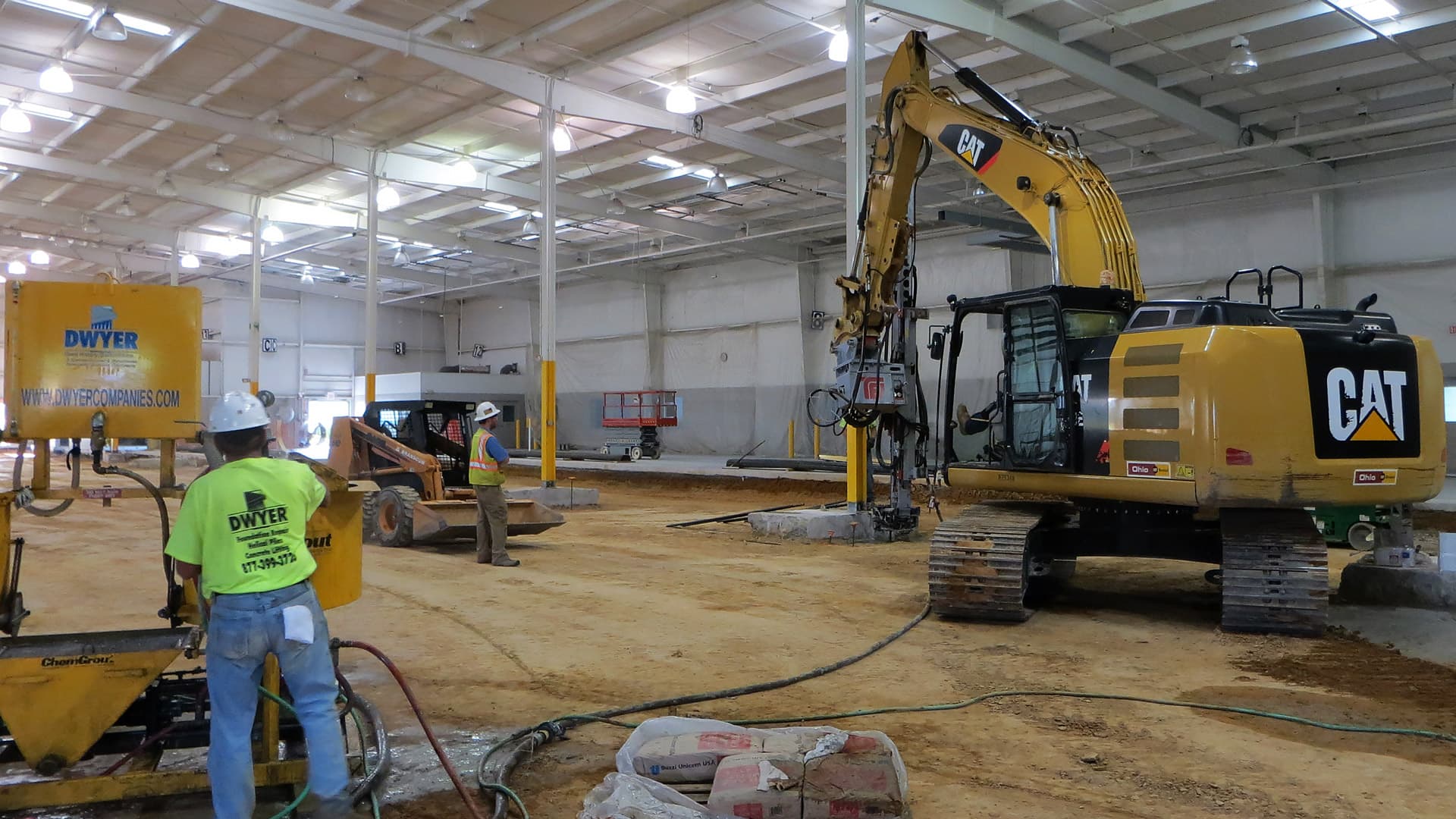 an image inside of a warehouse with a large Cat excavator and two workers in high vis vest
