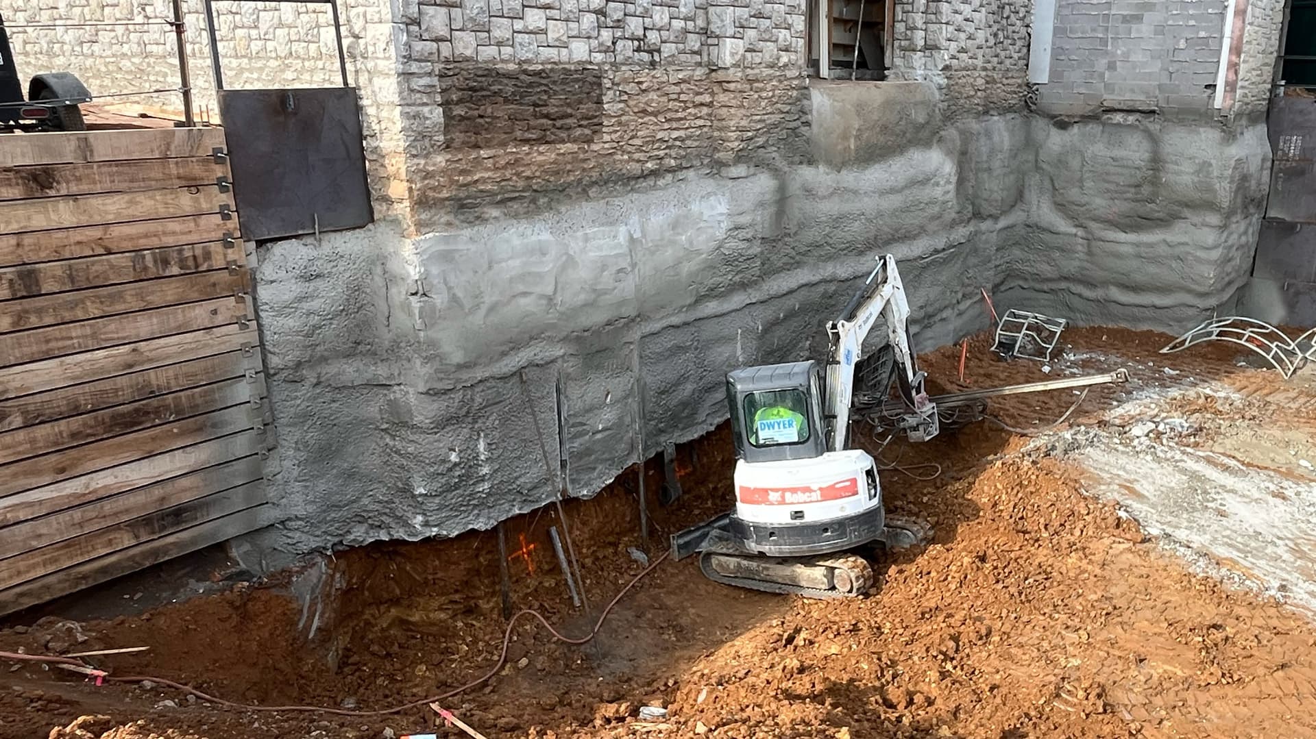 An image of the side of a commercial building being dug out by a bobcat excavator