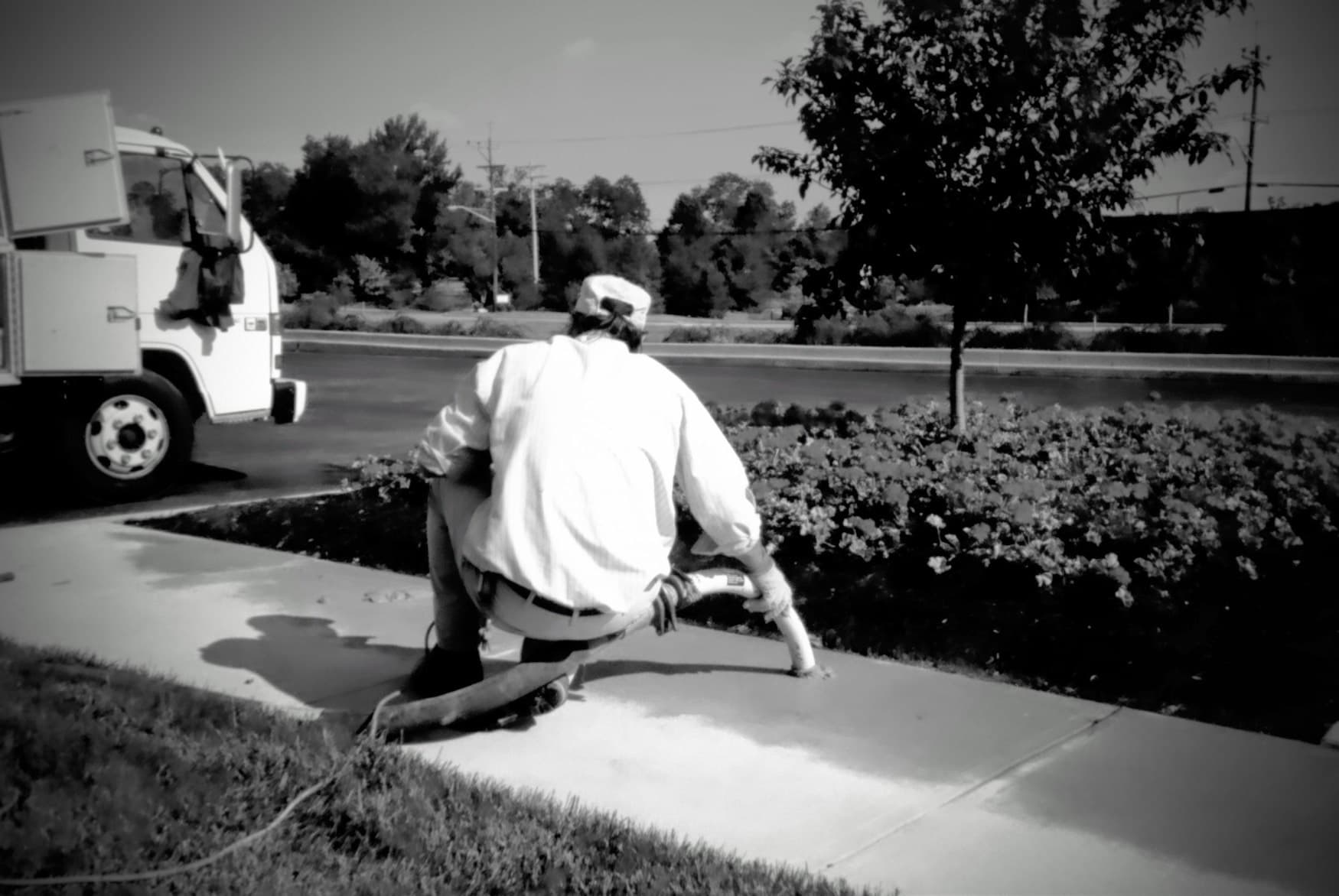 a black and white image of a worker lifting concrete on a sidewalk
