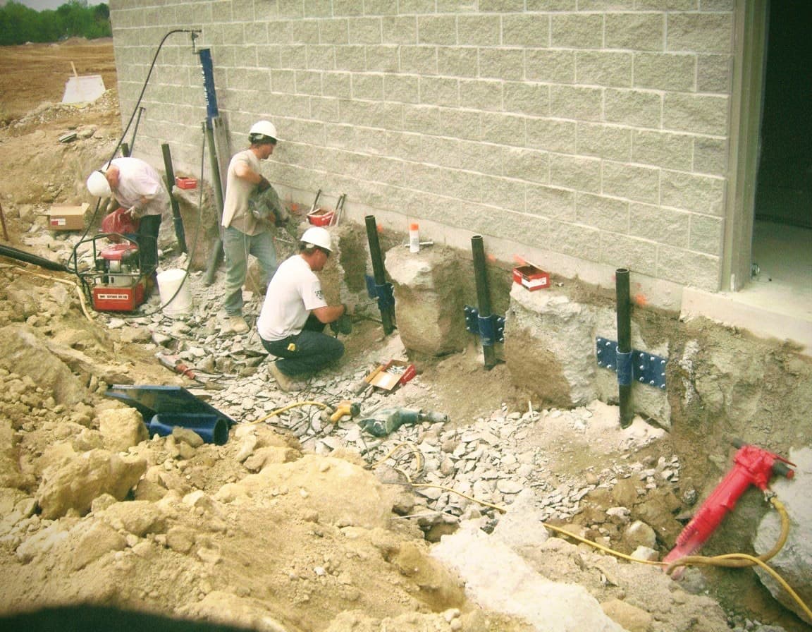 an image of three workers inserting ground supports at a foundation