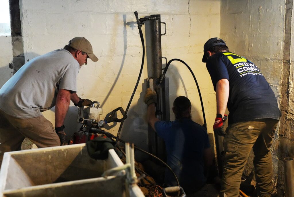 Three employees preforming foundation repair in a basement using piers